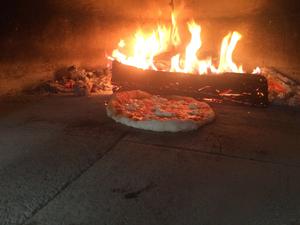 First Fire on the Bluff pizza baking Photo of interior of the oven with log fire and pizza baking.